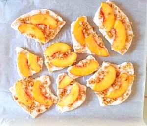 Frozen peach honey yoghurt bark broken into pieces on parchment paper